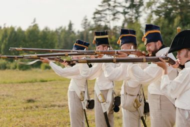 Soldiers in vintage uniforms aiming rifles during a historical battle reenactment outdoors.